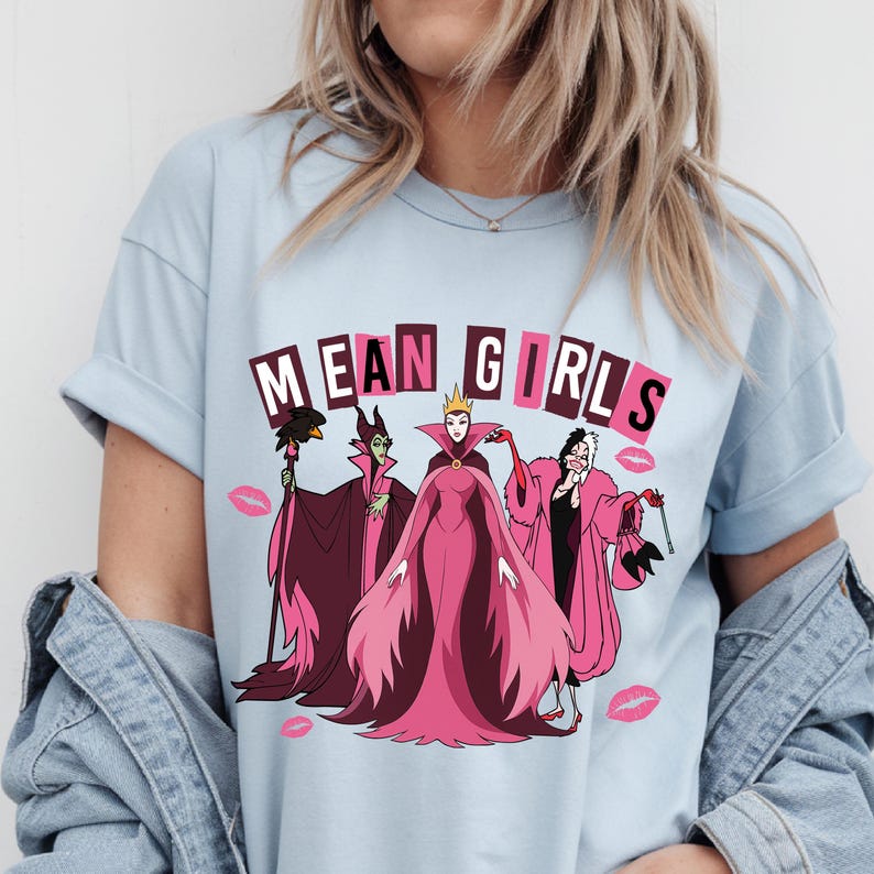 May include: Pale blue t-shirt with a graphic of four cartoon villains and the text "MEAN GIRLS" in pink and white. The design includes pink lipstick kiss marks.