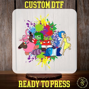 May include: A white sublimation blank featuring a colourful design of the characters from the film Inside Out. The characters are Joy, Sadness, Fear, Anger, and Disgust. The design includes colourful paint splatters. The text "CUSTOM DTF" is at the top of the blank and "READY TO PRESS" is at the bottom.