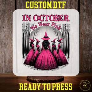 May include: A white square with a pink graphic of five witches in pink dresses and hats, with the text "IN OCTOBER We Wear Pink". The words "CUSTOM DTF" and "READY TO PRESS" are also displayed.