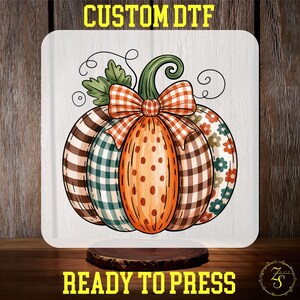 May include: A decorative pumpkin design with a variety of patterns, including plaid and floral, and a large orange bow. The pumpkin is on a white background with the text "CUSTOM DTF" and "READY TO PRESS".