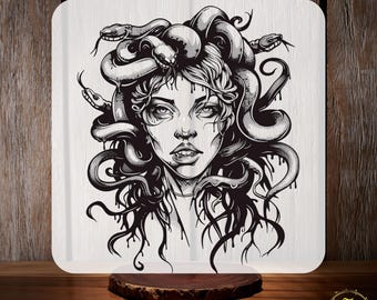 May include: A black and white illustration of Medusa with snakes for hair, printed on a white square. The text "CUSTOM DTF" is at the top, and "READY TO PRESS" is at the bottom. The image is on a wooden surface.