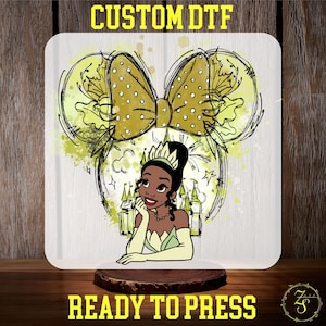 May include: A square, white graphic with a cartoon illustration of Princess Tiana, a gold bow with white polka dots, and the text "CUSTOM DTF" and "READY TO PRESS" in yellow.