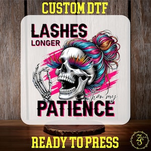 May include: A white square design transfer featuring a pink, blue and orange skull with long eyelashes. The skull is wearing a bun and the text reads "Lashes Longer Than My Patience".