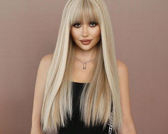 May include: A woman with long, straight, blonde hair with a light brown highlight. She is wearing a black tank top and a silver chain necklace with a safety pin pendant.