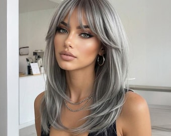 May include: A woman with long, layered, silver-gray hair with bangs. She is wearing a black tank top and gold hoop earrings. A silver chain necklace is around her neck. Her makeup includes eyeliner and lipstick.
