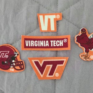May include: A collection of five embroidered patches featuring Virginia Tech branding. The set includes a maroon football helmet with a VT logo, a rectangular maroon patch with white text reading VIRGINIA TECH, a maroon turkey mascot, and two orange VT logos.