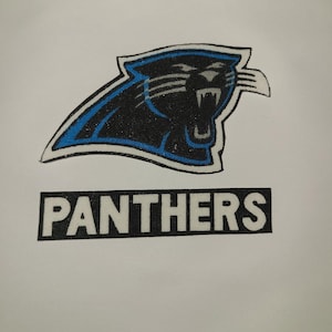 May include: A black and blue Carolina Panthers logo with the word "PANTHERS" in a black rectangle below. The logo features a panther head with its mouth open, outlined in blue.