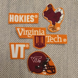 May include: A collection of orange and maroon Virginia Tech Hokies patches. The patches include the word "Hokies", "Virginia Tech", a turkey mascot, the letters "VT", and a football helmet. The patches are on a gray textured background.