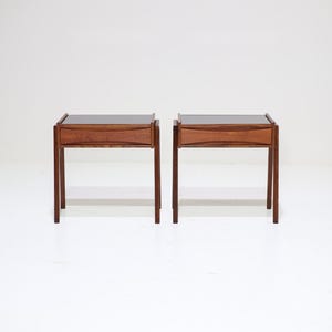 May include: Two matching mid-century modern nightstands. Each nightstand has a dark wood frame with a drawer and a dark, possibly black, top. The nightstands have four slender legs and are set against a white background.