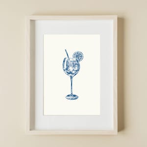 May include: A framed illustration of a blue cocktail with ice cubes and a lemon slice in a tall glass with a straw. The illustration is on a white background.