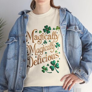 May include: A white t-shirt with the text "Magically Magically Delicious" in gold lettering and green shamrock designs.