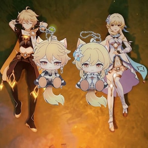 Puede incluir: Dos llaveros de personajes de dibujos animados de estilo chibi, uno masculino y otro femenino, cada uno con orejas de gato. El personaje masculino viste un atuendo oscuro con detalles dorados, mientras que el personaje femenino lleva un vestido blanco y azul. Ambos tienen pelo rubio y están en llaveros plateados.