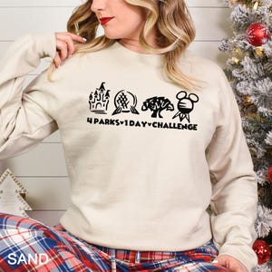 May include: A sand-colored sweatshirt with a black graphic design featuring four iconic park symbols and the text "4 Parks 1 Day Challenge." The long-sleeved top is made of a soft material.