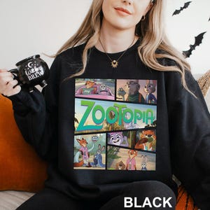 May include: Black sweatshirt featuring a colorful graphic from the animated film "Zootopia." The design includes various characters and the film's title in a vibrant font. The word "BLACK" is printed at the bottom.