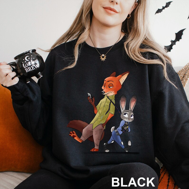 May include: Black sweatshirt featuring a cartoon illustration of a fox and a rabbit. The fox is wearing a green shirt and brown pants, while the rabbit is in a blue uniform. The word "BLACK" is printed at the bottom.