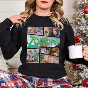 May include: Black crewneck sweatshirt featuring a colorful graphic from the animated film "Zootopia." The design includes the film's title in green and images of the characters. The word "BLACK" is printed at the bottom.