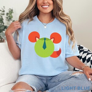 May include: Light blue t-shirt featuring a cartoon mouse design with a green face, orange ears, and a blue tie. The shirt is made of a soft material and is suitable for casual wear. The text "LIGHT BLUE" is printed at the bottom.
