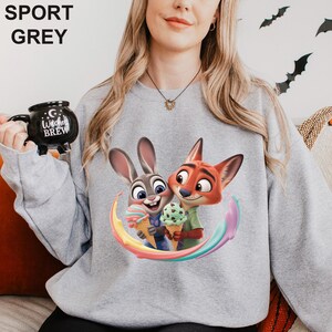 May include: Sport grey sweatshirt featuring a colorful graphic of a bunny and fox holding ice cream cones. The sweatshirt has the words "SPORT GREY" printed at the top. The characters are set against a rainbow swirl.