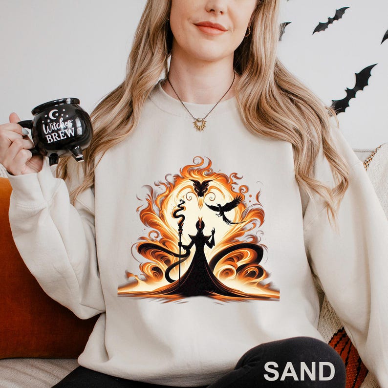 Op de afbeelding: Zandkleurige sweatshirt met een opvallende afbeelding van een tovenaar met staf, tegen een vurige oranje achtergrond met zwarte vogels. De sweatshirt heeft een ronde hals en lange mouwen. Een zwarte mok met de tekst "Witches Brew" wordt in de afbeelding vastgehouden.
