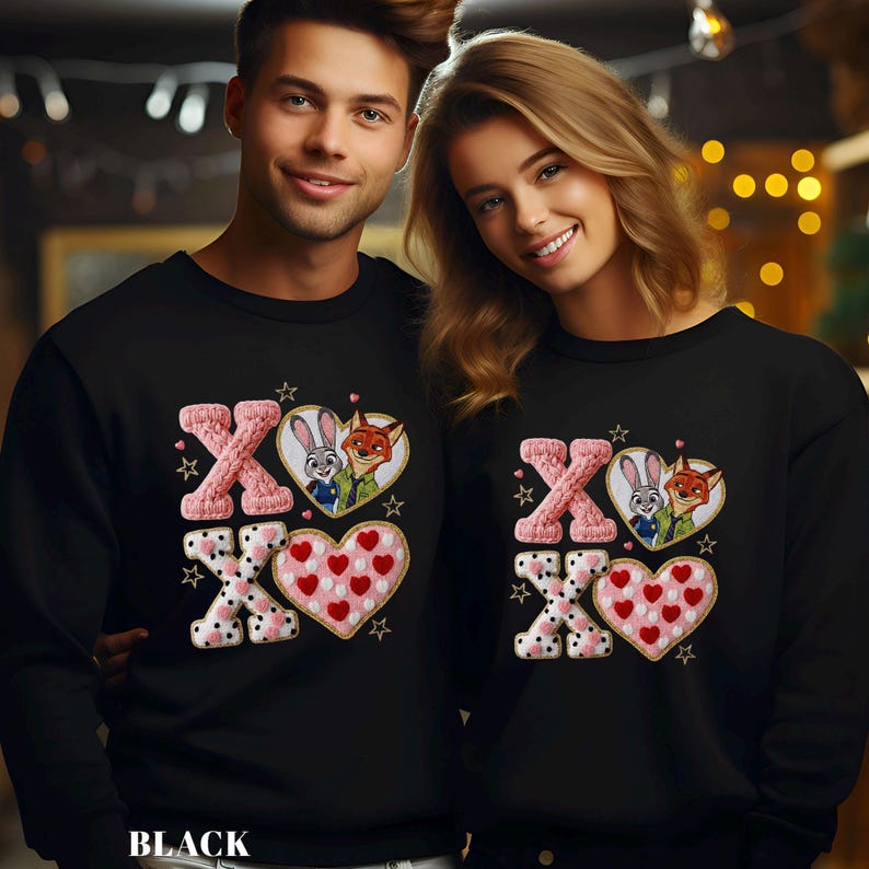 May include: Black sweatshirts with a Valentine's Day design. The design includes the letters "XO", hearts, and images of cartoon characters. The sweatshirts are worn by two people.