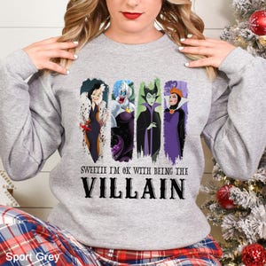 May include: Sport grey sweatshirt featuring four cartoon villain characters with the text "Sweetie I'm ok with being the Villain". The sweatshirt is a long-sleeved crew neck.