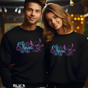 May include: Black sweatshirts with the word "Ohana" in blue and purple script, accompanied by a cartoon character playing a guitar. The sweatshirts are worn by two people. The word "BLACK" is printed at the bottom.