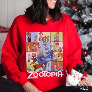 May include: A red sweatshirt featuring a colorful graphic of characters from the animated film "Zootopia." The design includes a grid of images and the word "Zootopia" in white. The sweatshirt is a solid red color.