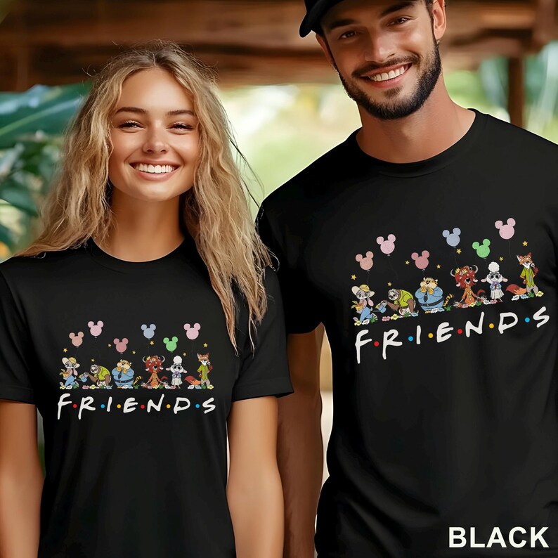 Puede incluir: Camisetas negras con un dise&ntilde;o de dibujos animados con varios personajes y la palabra "FRIENDS" en blanco. Encima de los personajes hay siluetas de cabezas de Mickey Mouse de colores. La palabra "BLACK" est&aacute; impresa en la parte inferior derecha.