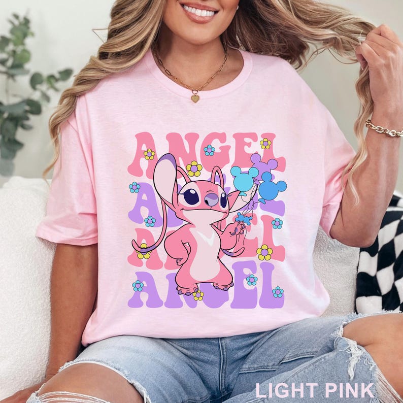 May include: Light pink t-shirt featuring a cartoon character with the word "ANGEL" in a retro font. The design includes flowers and the text "LIGHT PINK" at the bottom. The character is holding blue balloons.