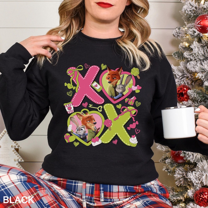 Peut inclure: Sweat-shirt noir avec un motif rose et vert repr&eacute;sentant Nick Wilde et Judy Hopps de Zootopie. Le motif comprend les lettres "X" et "O", des c&oelig;urs et d'autres &eacute;l&eacute;ments d&eacute;coratifs. Le mot "BLACK" est imprim&eacute; en bas.