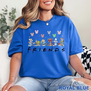 Puede incluir: Camiseta azul real con un dise&ntilde;o de dibujos animados de varios personajes de animales sosteniendo globos de Mickey Mouse. La palabra "FRIENDS" est&aacute; impresa en una fuente colorida. Un estilo casual y c&oacute;modo.