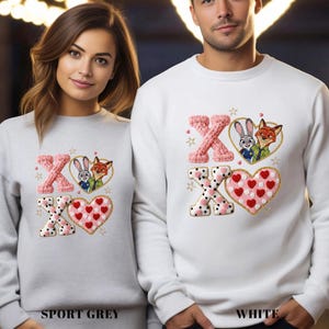 May include: Sport grey and white sweatshirts with an embroidered design. The design features the letters "XO", a heart, and cartoon characters. The heart is pink with red hearts. The text "SPORT GREY" and "WHITE" are at the bottom.