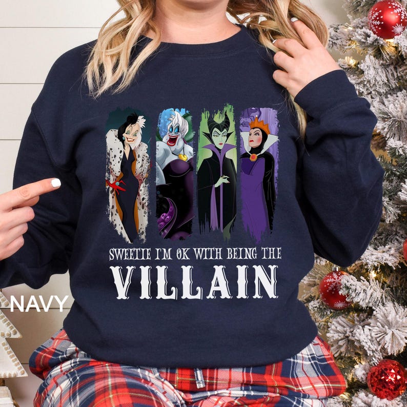 May include: Navy blue sweatshirt featuring four cartoon villains: Cruella de Vil, Ursula, Maleficent, and the Evil Queen. The text "Sweetie I'm OK with being the Villain" is printed below the characters in white. The word "NAVY" is printed on the left side.