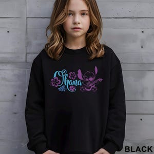 May include: Black sweatshirt featuring the word "Ohana" in blue and purple script, with floral accents and a cartoon character playing a ukulele. The word "BLACK" is printed in white at the bottom right.