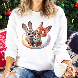 May include: White sweatshirt featuring a colorful cartoon image of a bunny and fox holding ice cream cones. The bunny is gray and the fox is orange. The ice cream cones have pastel colors. The sweatshirt is a crew neck style.