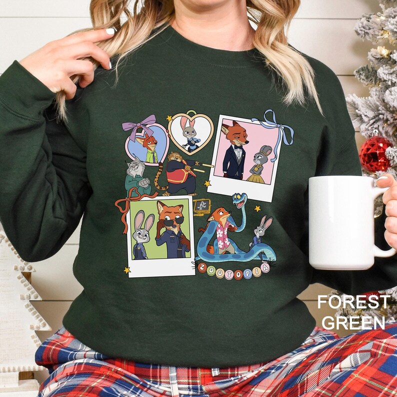 May include: Forest green sweatshirt featuring cartoon characters from Zootopia. The design includes polaroid-style images of Nick Wilde and Judy Hopps, along with other characters. The sweatshirt is a solid color with the words "Forest Green" printed at the bottom.
