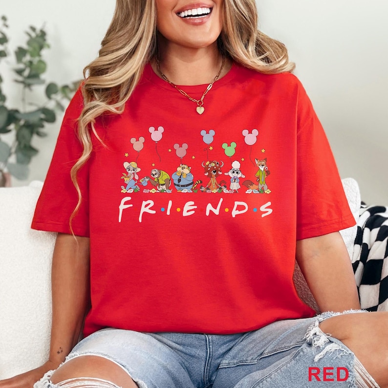Puede incluir: Una camiseta roja con la palabra "FRIENDS" en blanco, personajes de dibujos animados y gr&aacute;ficos de globos de Mickey Mouse. La camiseta es de color rojo vibrante y tiene un corte holgado.