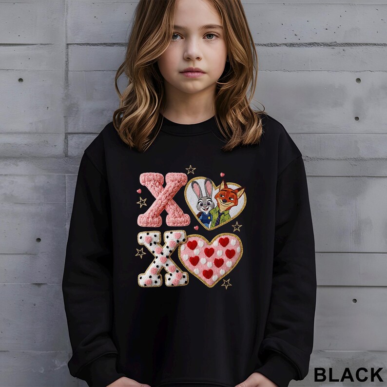 May include: Black sweatshirt featuring the text "XO" with heart and star designs. The "X" letters are pink, one knitted and the other with a polka dot pattern. The "O" letters are heart-shaped, one with a cartoon bunny and fox, the other with red hearts.