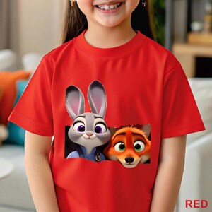 May include: A red t-shirt featuring a graphic of Judy Hopps and Nick Wilde from Zootopia. The cartoon characters are depicted with detailed facial features. The word "RED" is printed in the bottom right corner.