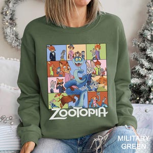 May include: Military green sweatshirt featuring a colorful graphic of characters from the animated film "Zootopia." The design includes various animal characters in a grid pattern, with the film's title in white block letters at the bottom.