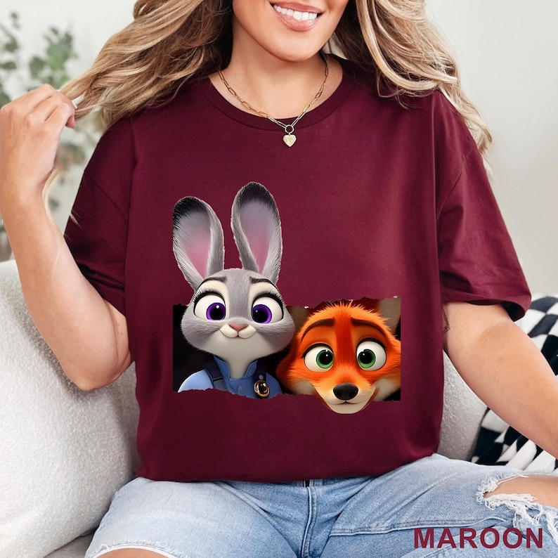 May include: Maroon t-shirt featuring a graphic of Judy Hopps and Nick Wilde from Zootopia. The cartoon characters are set against a black background. The word "MAROON" is printed in white at the bottom right.
