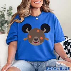 May include: Royal blue t-shirt featuring a cartoon character with large black ears, brown fur, and orange flower accents. The character has a smiling face with two white teeth. The text "ROYAL BLUE" is at the bottom of the image.