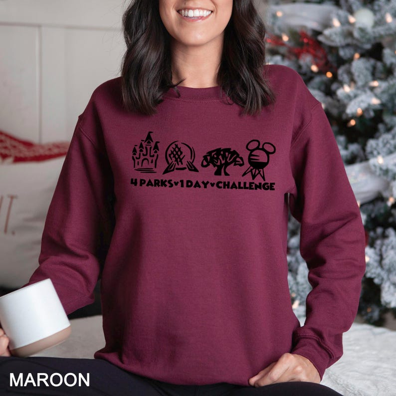 May include: Maroon sweatshirt with a black graphic featuring four theme park icons and the text "4 Parks 1 Day Challenge." The sweatshirt is a solid maroon color and has a crew neck.