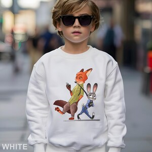 May include: White sweatshirt featuring a cartoon illustration of Nick Wilde and Judy Hopps from Zootopia. Nick, an orange fox, is holding a phone, while Judy, a gray rabbit, walks beside him. The word "WHITE" is printed at the bottom.