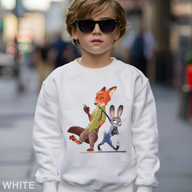 May include: White sweatshirt featuring a cartoon illustration of Nick Wilde and Judy Hopps from Zootopia. Nick, an orange fox, is holding a phone, while Judy, a gray rabbit, walks beside him. The word "WHITE" is printed at the bottom.