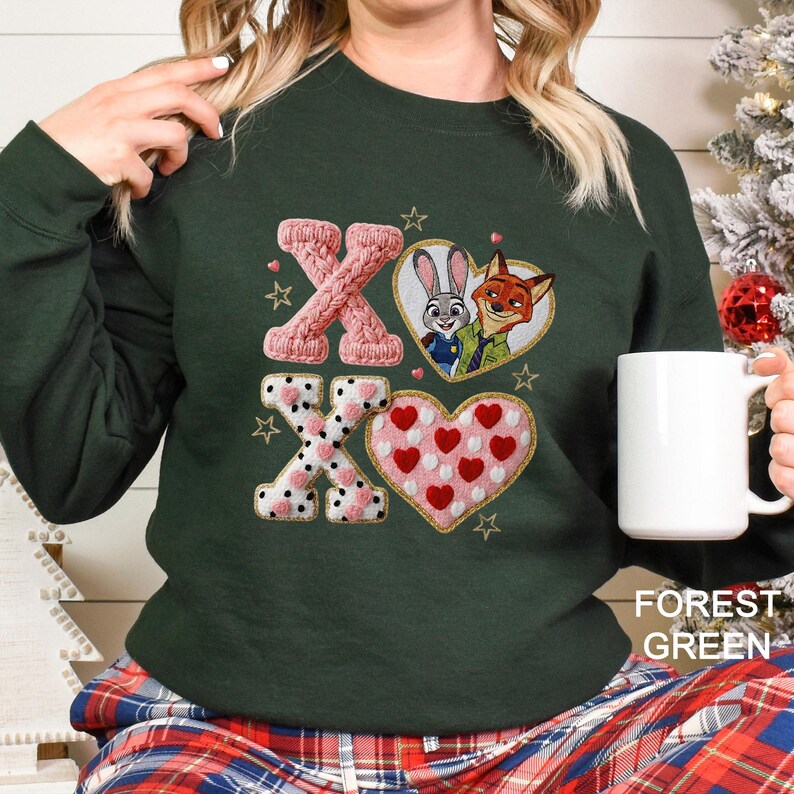 May include: Forest green sweatshirt with embroidered "XO" design. The "X"s are pink, one knitted and the other with white polka dots. A heart with red hearts and a heart with the Zootopia characters are also featured. The text "FOREST GREEN" is at the bottom.