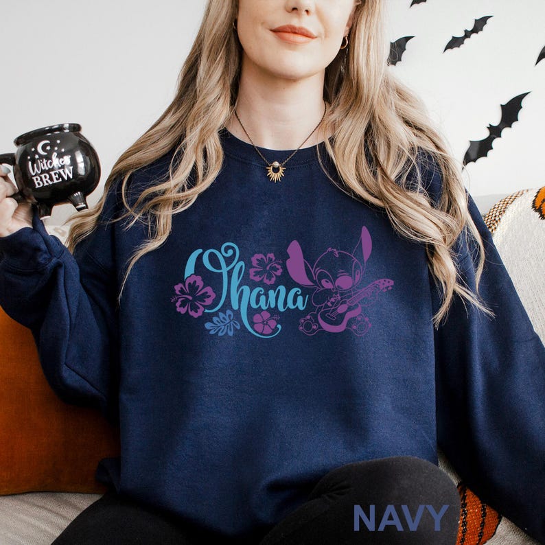 May include: Navy blue sweatshirt featuring the word "Ohana" in teal and purple, with a floral design and a cartoon character playing a ukulele. The word "NAVY" is printed in white at the bottom of the sweatshirt.