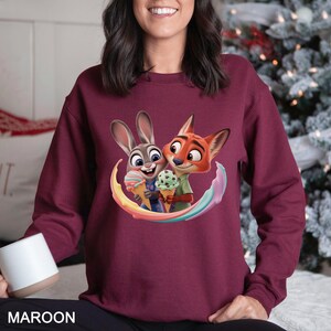 May include: Maroon sweatshirt featuring a colorful graphic of a bunny and fox holding ice cream cones. The cartoon characters are surrounded by a rainbow arc. The word "MAROON" is printed at the bottom of the sweatshirt.