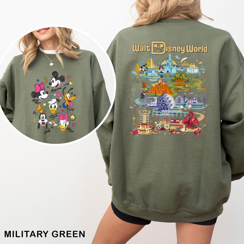 May include: Military green sweatshirt featuring a colorful graphic of Disney characters on the front, including Mickey Mouse, Minnie Mouse, Donald Duck, and Goofy. The back of the sweatshirt displays a detailed illustration of Walt Disney World with the text "Walt Disney World".