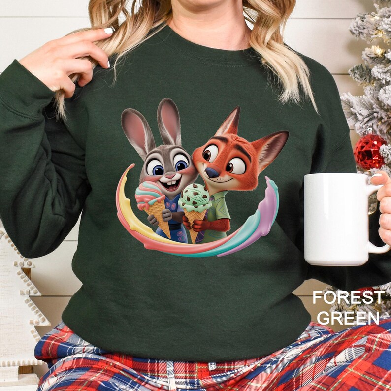May include: Forest green sweatshirt featuring a colorful graphic of Judy Hopps and Nick Wilde from Zootopia holding ice cream cones. The design is surrounded by a rainbow arc. The text "FOREST GREEN" is printed at the bottom right.